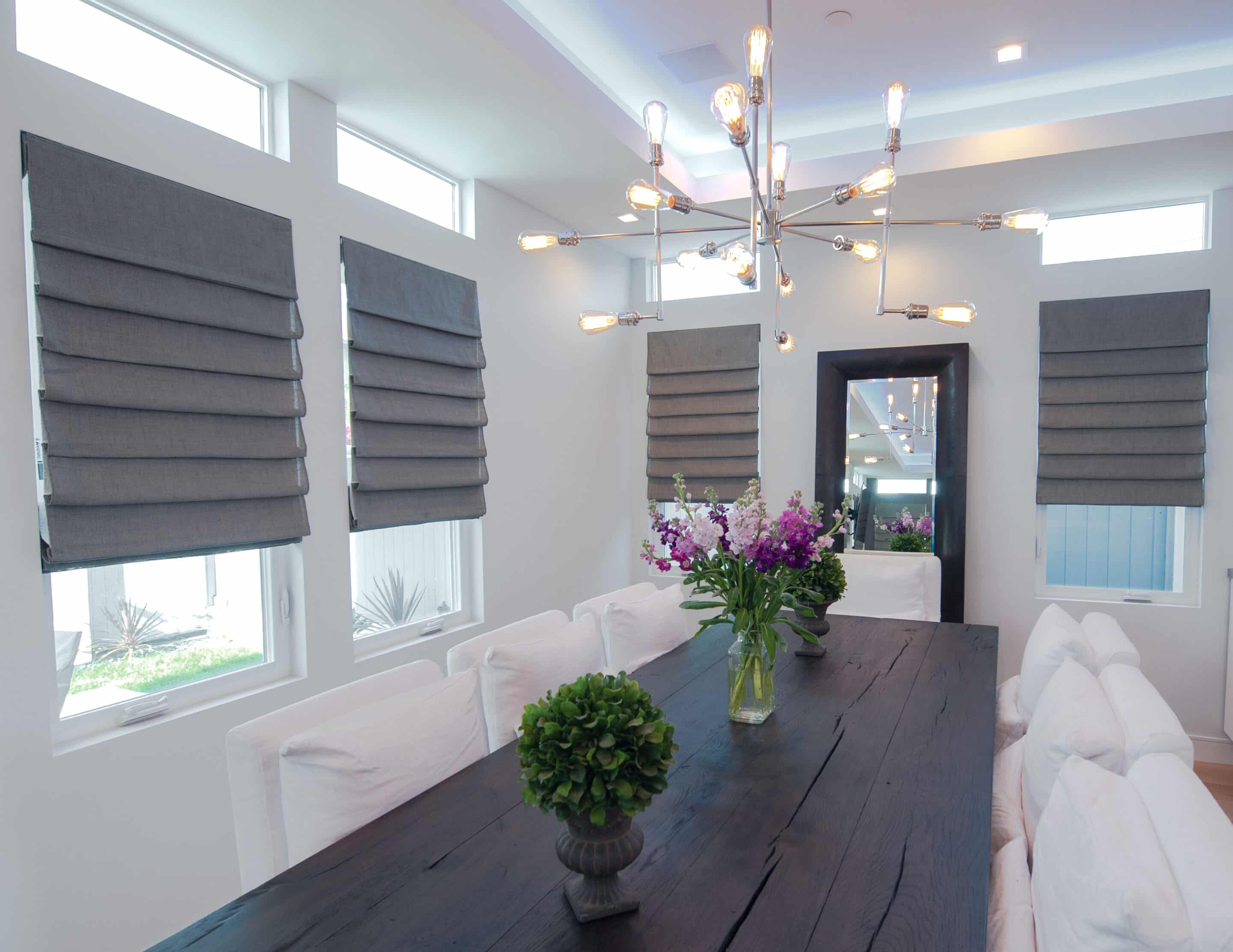 Grey Roman shades covering windows in a large dining room.