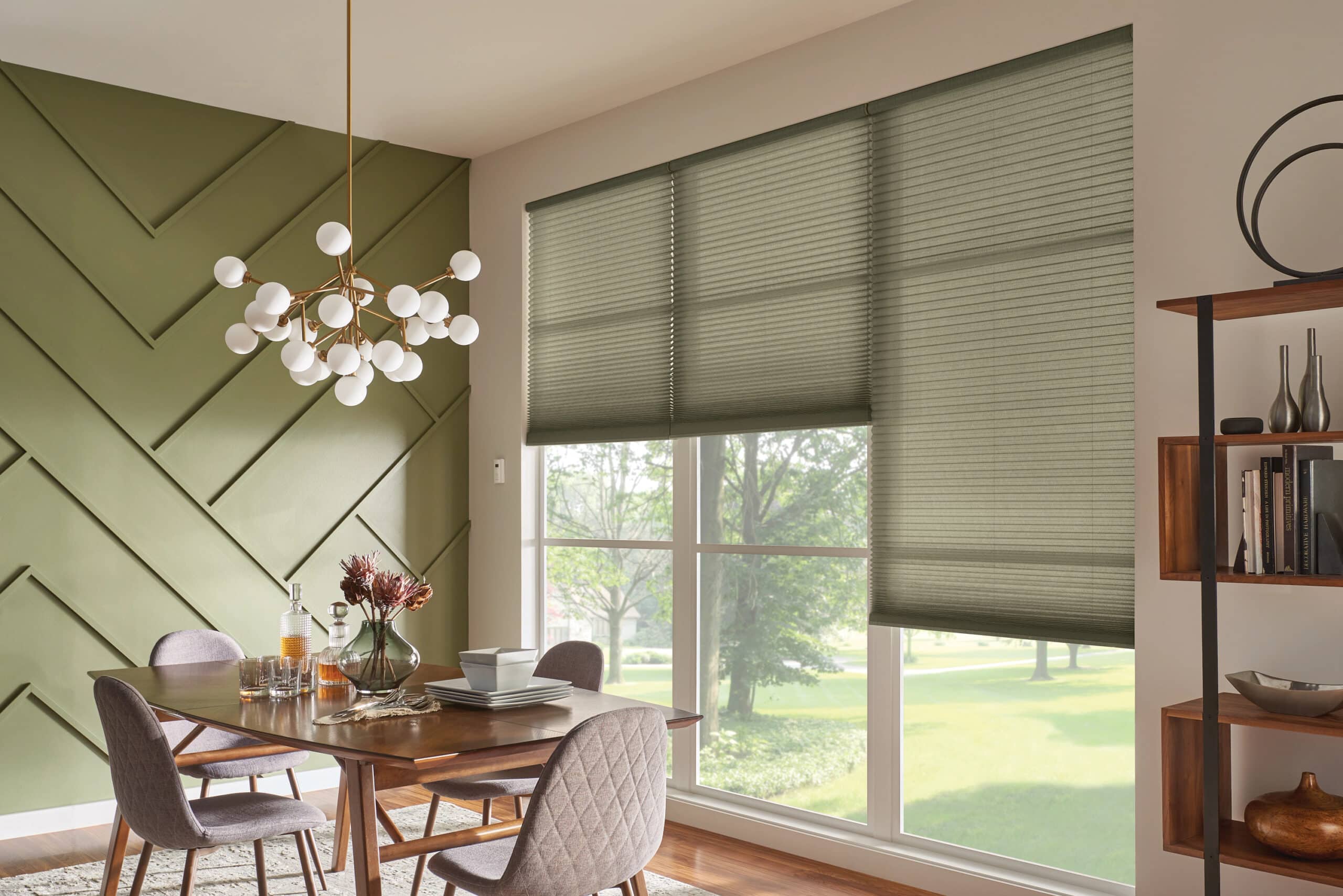 Dining room with large windows fitted with green cellular shades, letting in soft natural light.