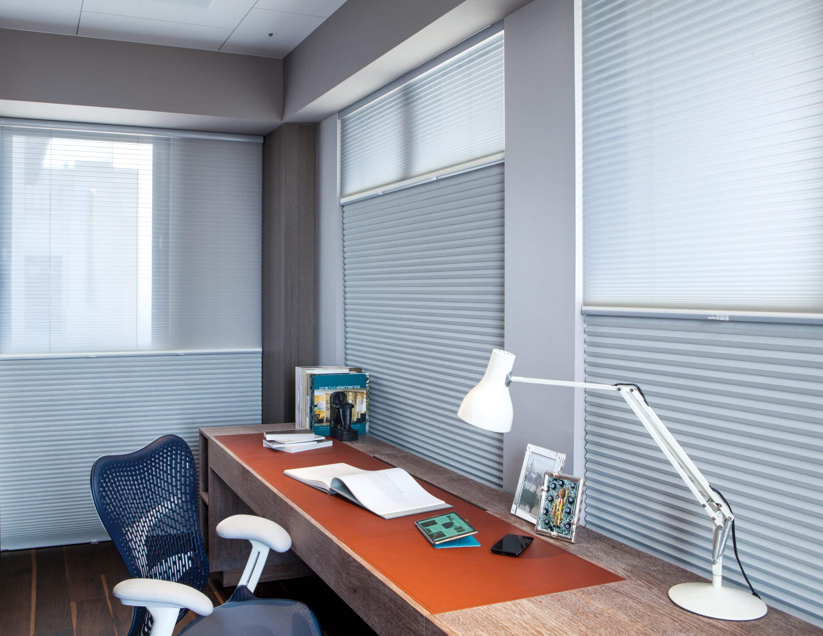 Home office with large windows covered by light filtering cellular shades in a top down bottom up style.